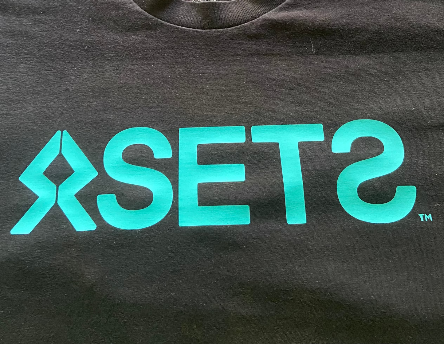 Two black t-shirts with 'ASETS' logo on a gray surface